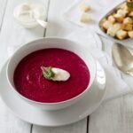 Vibrant crimson beetroot soup garnished with fresh herbs in white bowl, rich in natural nitrates for improved blood flow and sustained energy