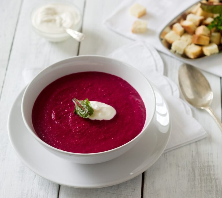 Vibrant crimson beetroot soup garnished with fresh herbs in white bowl, rich in natural nitrates for improved blood flow and sustained energy