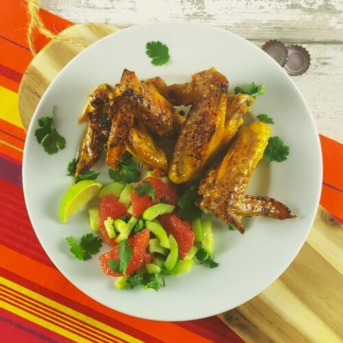 ginger marinated chicken wings tieh grapefruit and cucumber salad on a white plate