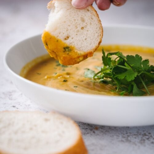 carrot and coriander [cilantro] soup with fresh bread in a white bowl