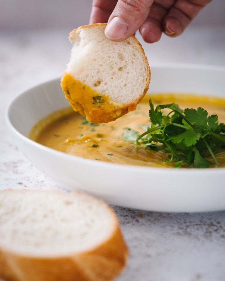 carrot and coriander [cilantro] soup with fresh bread in a white bowl