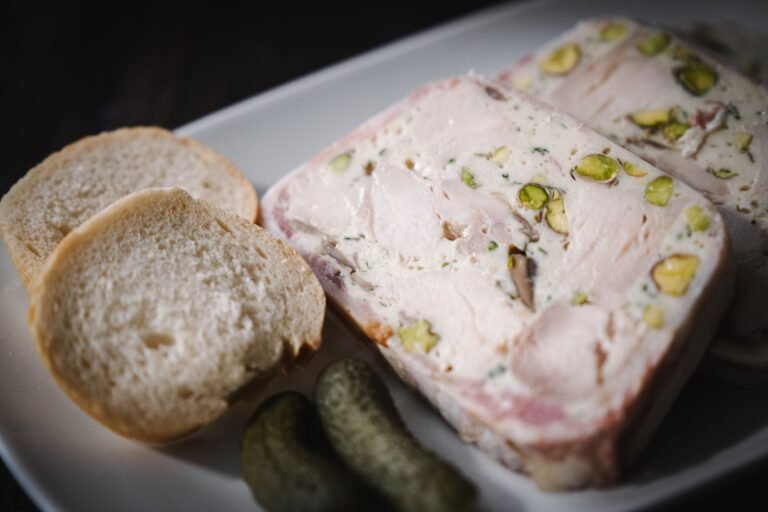 Slices of chicken and pistachio terrine on a plate with baguette slices and a cornichon