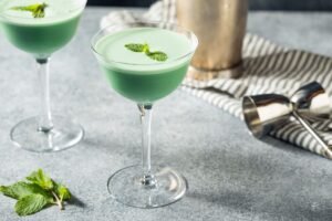 Grasshopper cocktail in a coupe glass on a table with a shaker for stocking a home bar