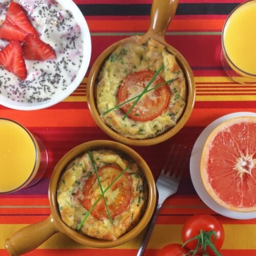 Baked eggs with mushrooms and bacon in ramekins with orange juice, a grapefruit half and yoghurt on a table
