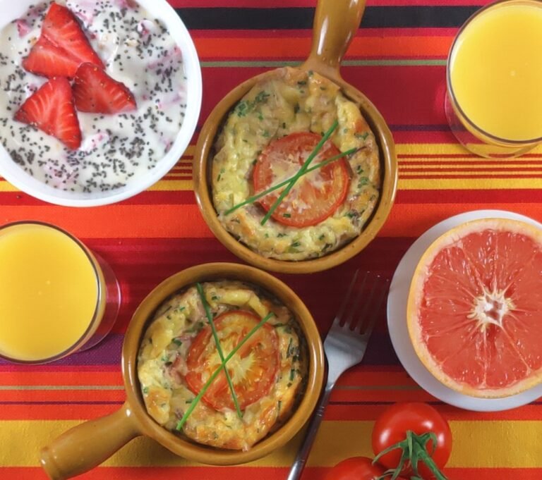 Baked eggs with mushrooms and bacon in ramekins with orange juice, a grapefruit half and yoghurt on a table
