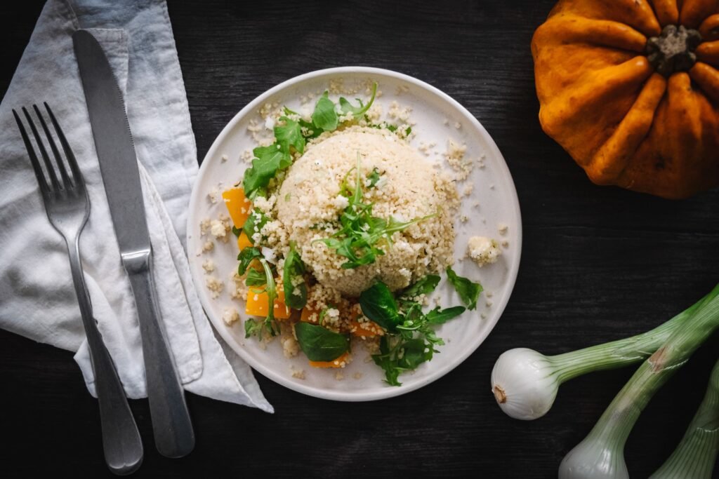 Roast Pumpkin Cous vegetarian Cous Salad with spring onion, chickpeas, arugula on a white plate