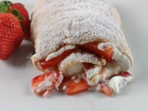 strawberry meringue roulade filled with fresh strawberries and creamy filling rolled then dusted with powdered sugar