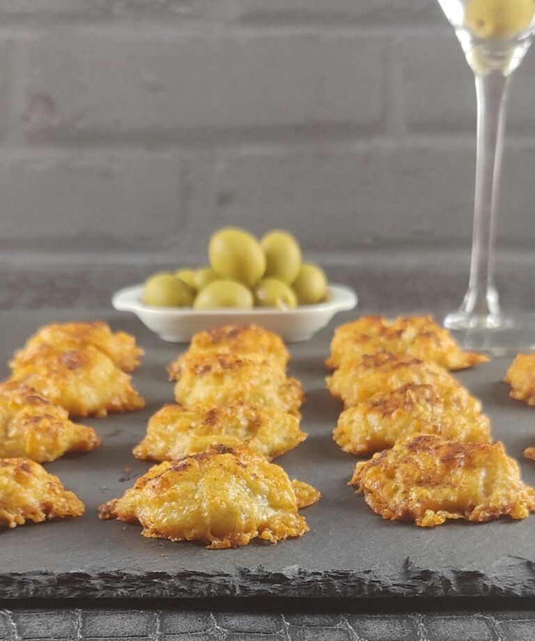 Gruyere cheese puffs on a tray with olives and a martini in the background