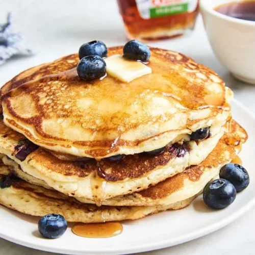 Blueberry pancakes on a plate with a cup of coffee and a bottle of maple syrup
