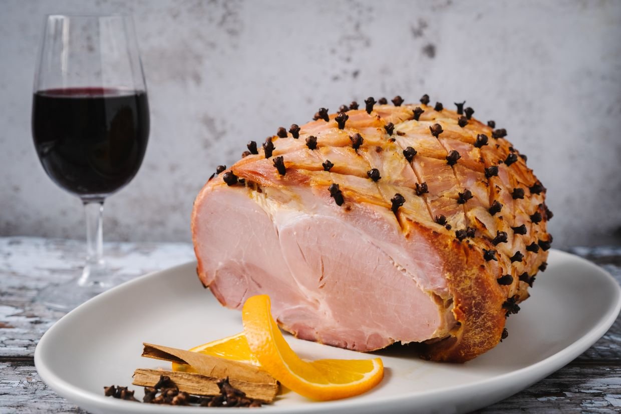 Honey glazed ham slided on a plate with a glass of red wint