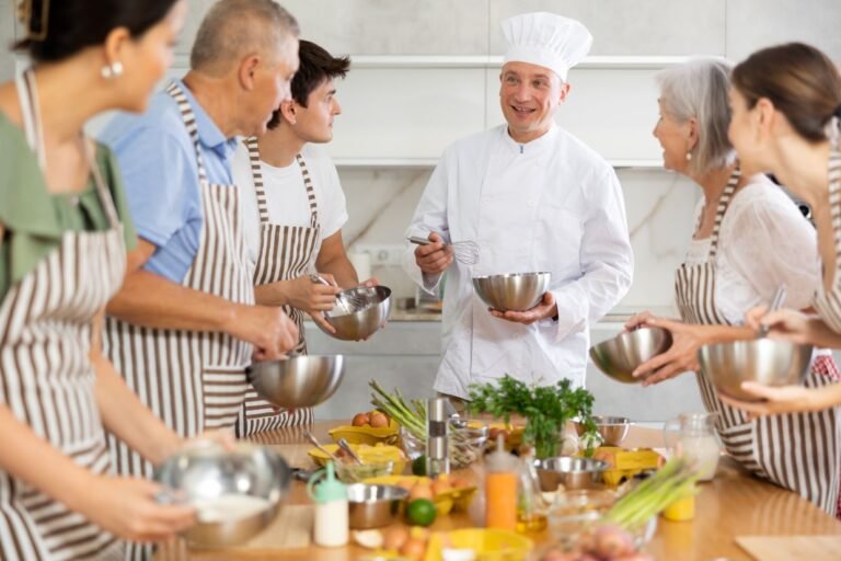 Cooking course - senior male chef in cook uniform teaches young people cooking class students to prepare and mix ingredients for dishes in restaurant By JackF