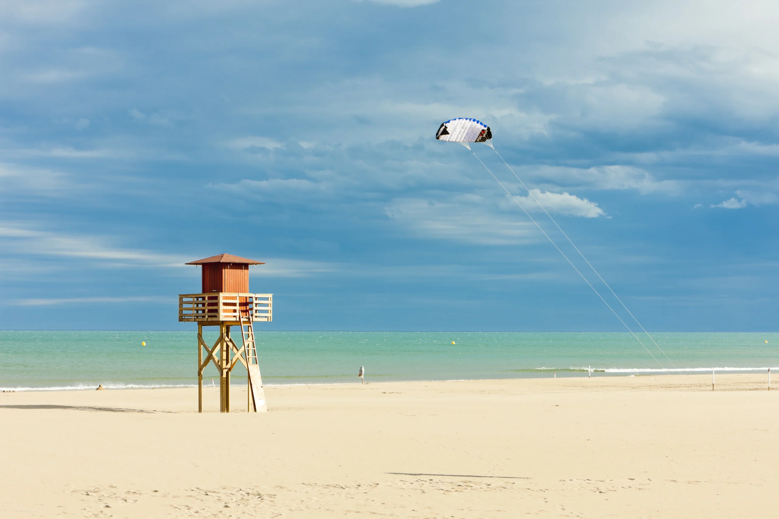 soaking up the sun on a mediterranean beach at Narbonne beach with lifesaver tower and windsurfer