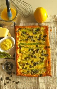 Asparagus, cheese and pumpkin seed tart on a cooling rack with lemons, mustard and butter i the background for Maison Bonhomie