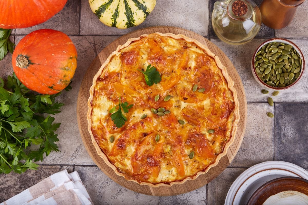 an uncut pumpkin tart on a board with pumpkin seeds