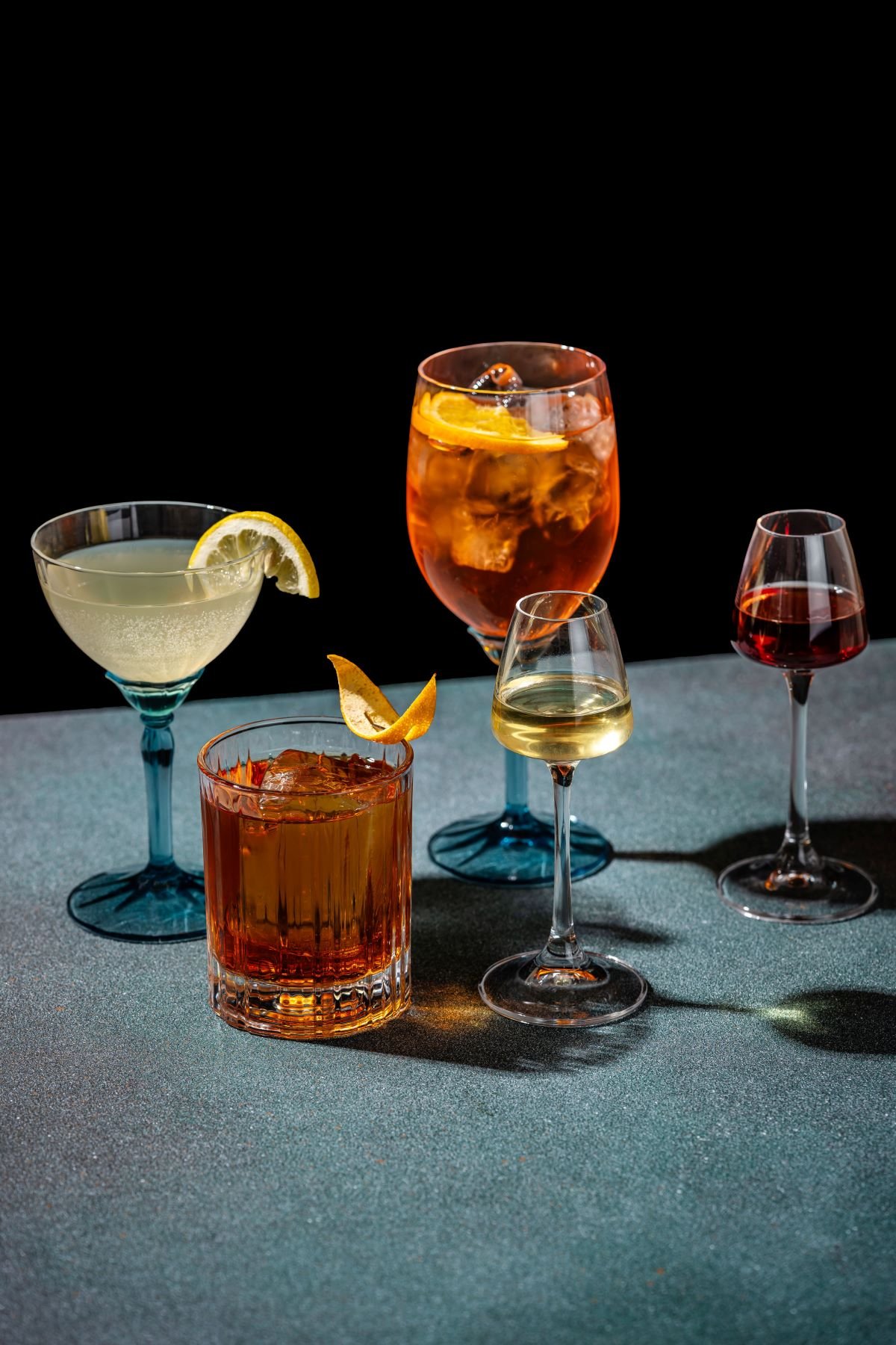 a selection of apertifs and digestifs with garnish on a dark background