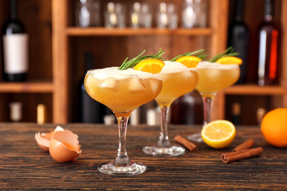 3 The godfather Sour cocktails with orange and rosemary garnish on a wooden bar